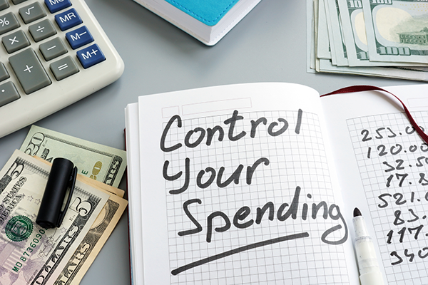 Notebook with Control Your Spending beside a calculator, pen, and cash, illustrating budgeting and finance management.
