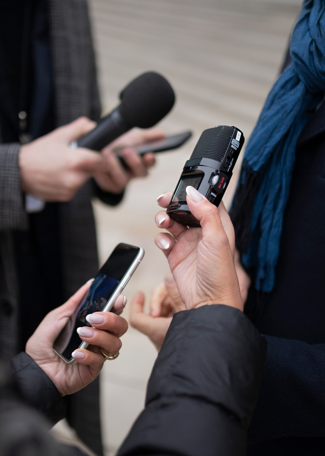Journalists conducting an outdoor interview with microphones and a smartphone.