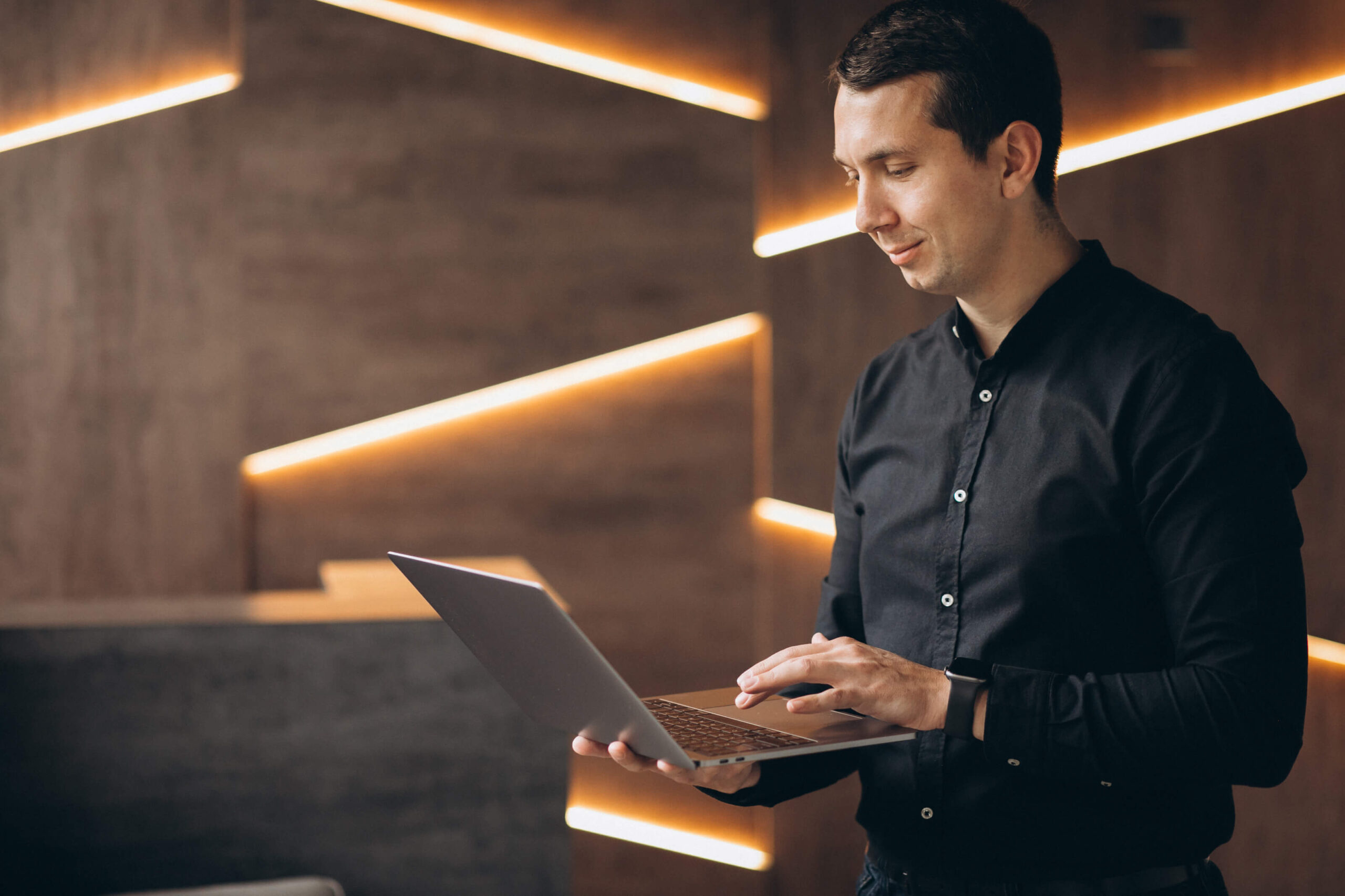 Man in black shirt using laptop in modern office with stylish lighting.