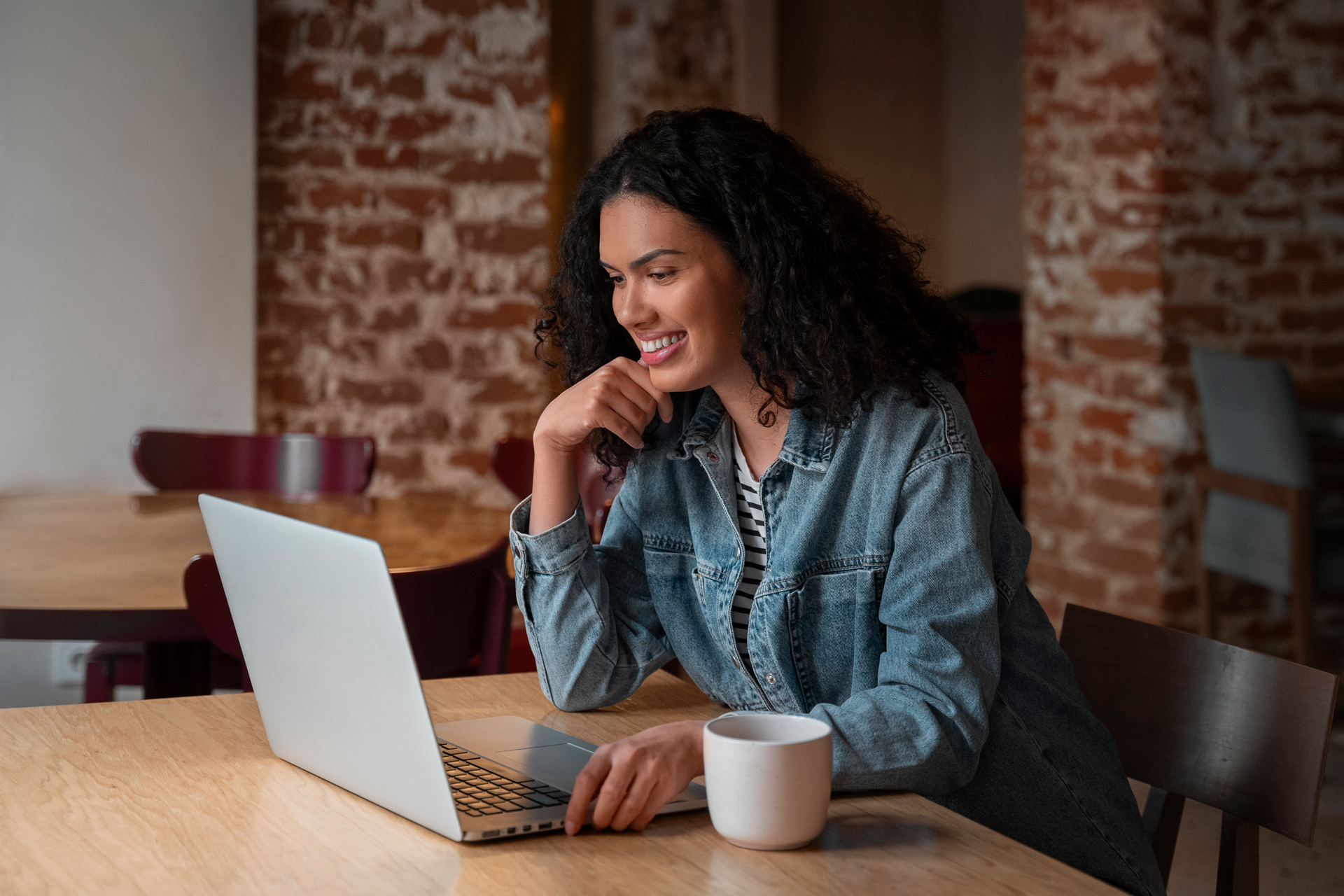 Smiling woman using laptop in cozy cafe, enjoying coffee and browsing online.