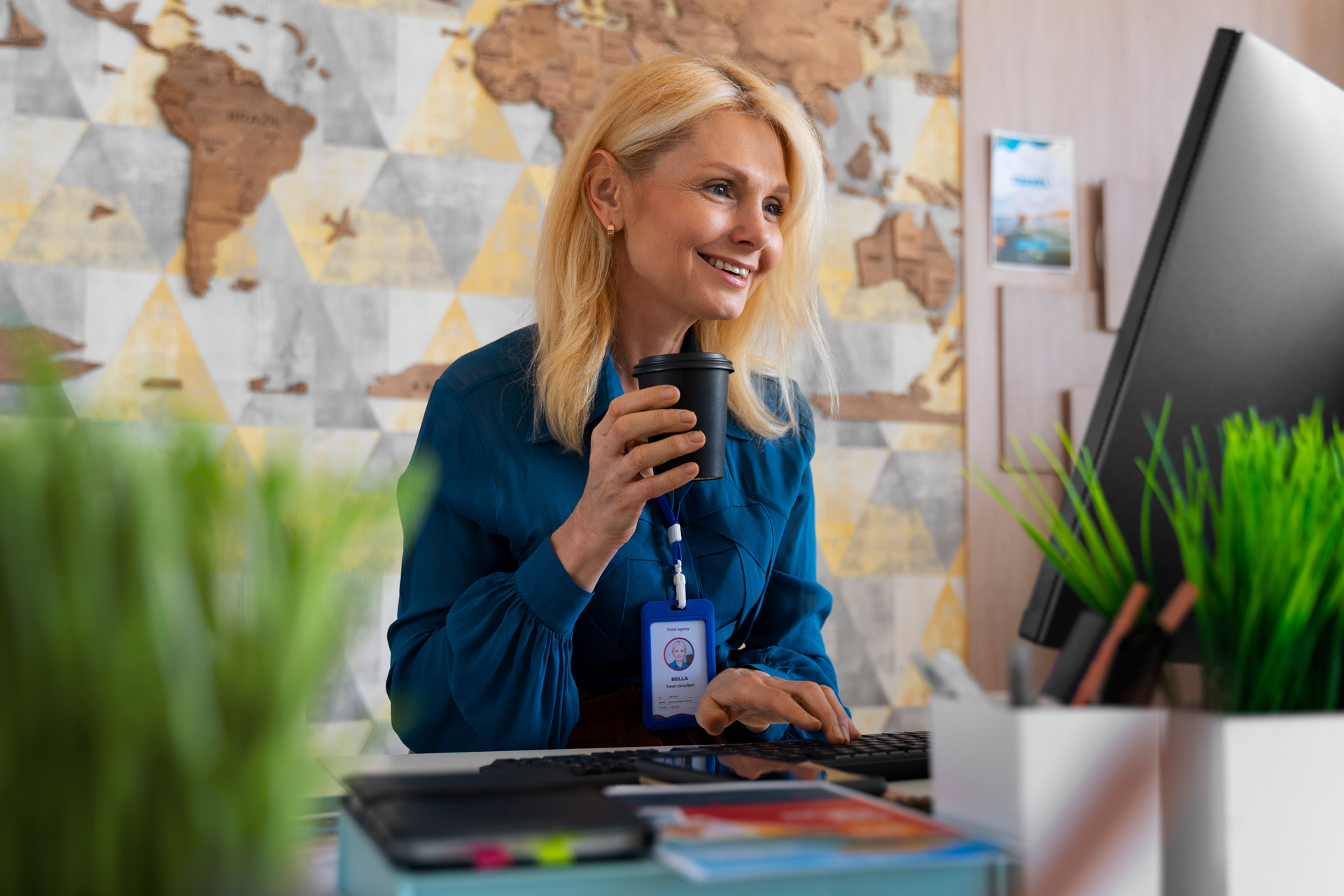 Smiling woman works at a computer holding coffee, with a world map in the background.