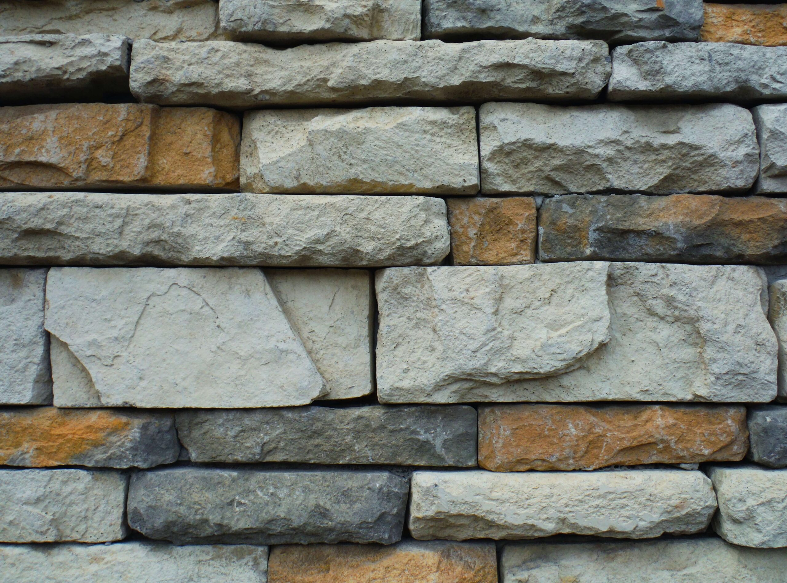 Rough stone wall texture with layered gray and tan bricks, ideal for natural building materials or architectural design.