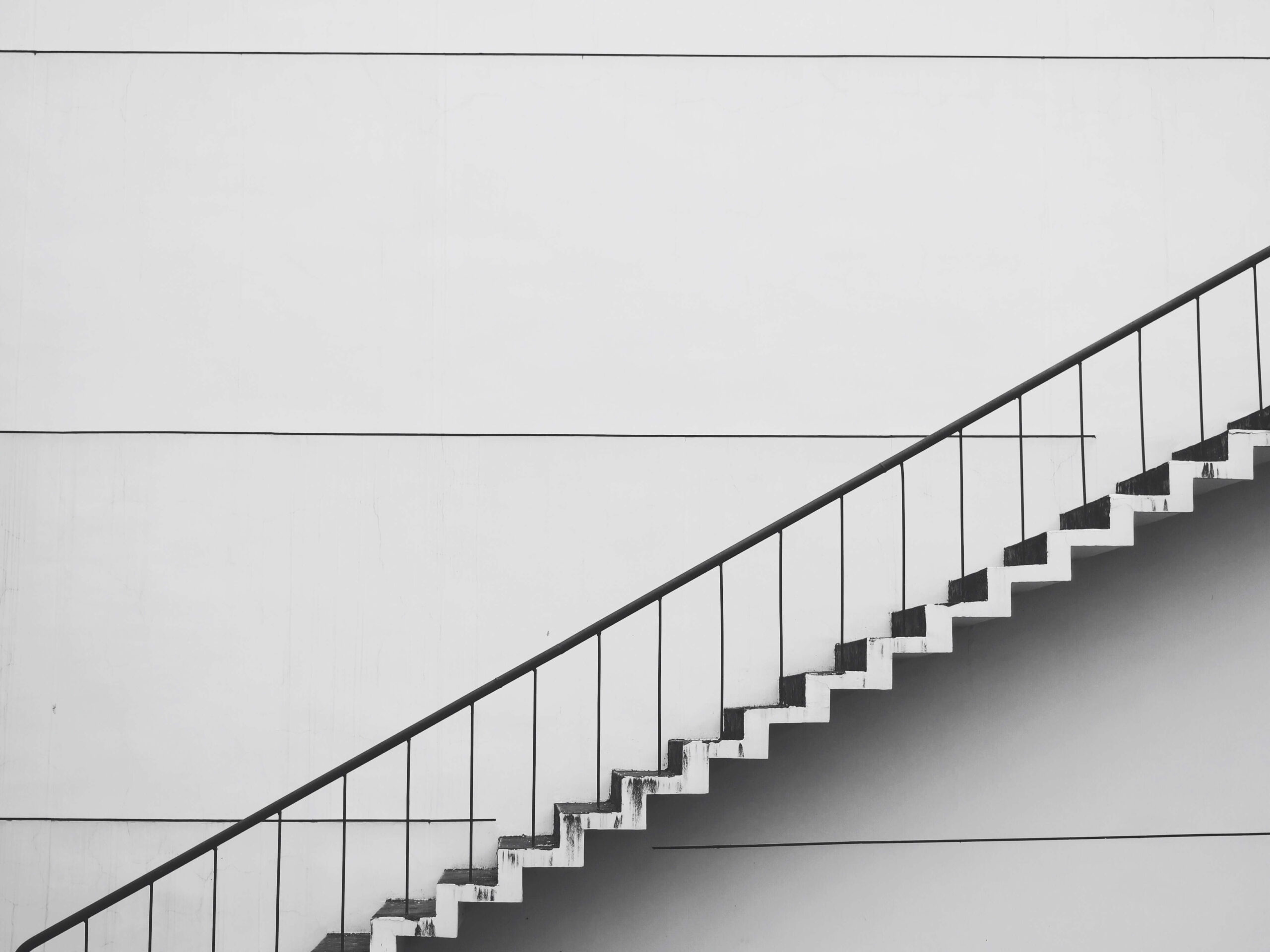 Modern minimalist staircase against a white wall, showcasing geometric lines and architectural simplicity.