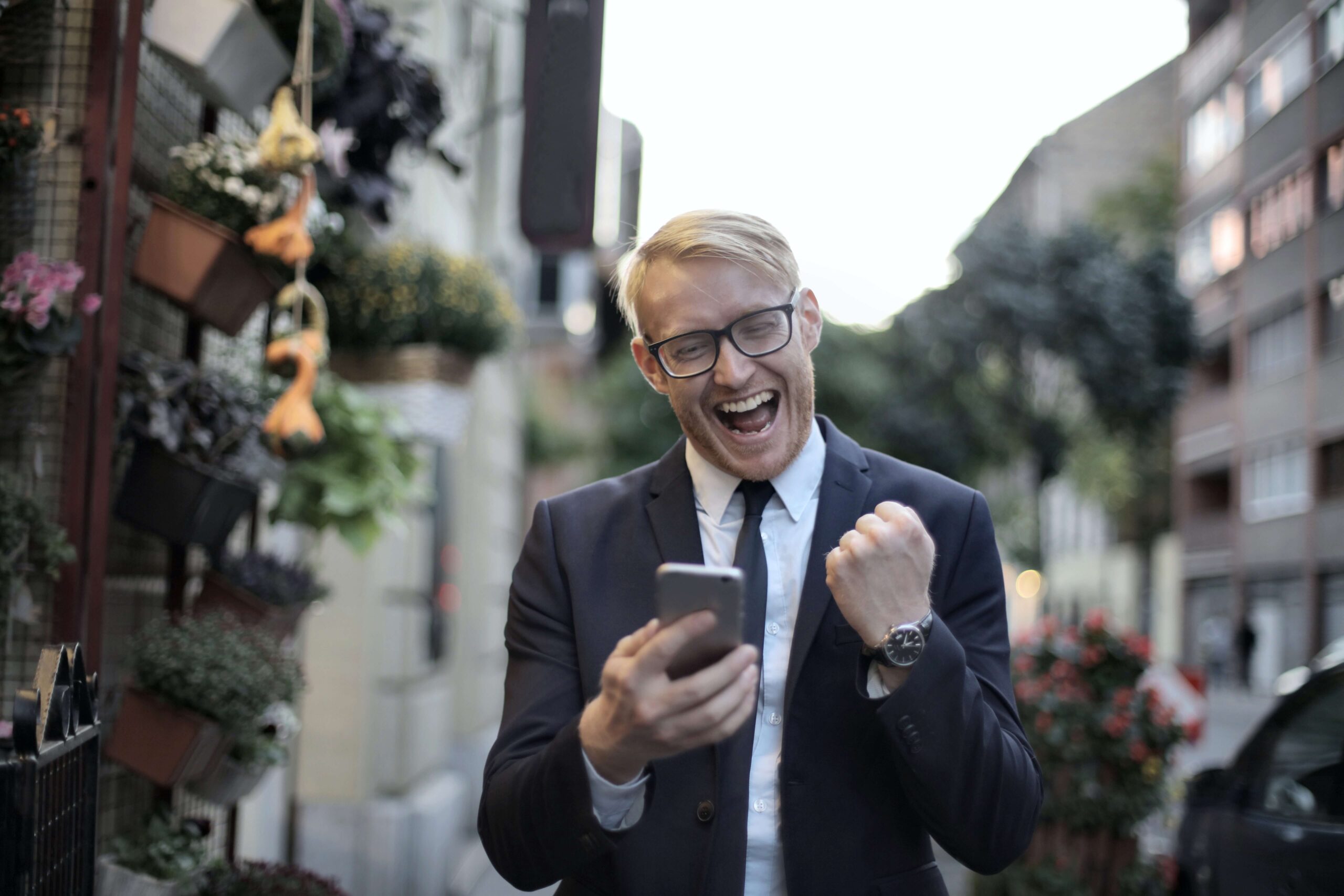 Man in suit celebrating success while looking at smartphone on city street.