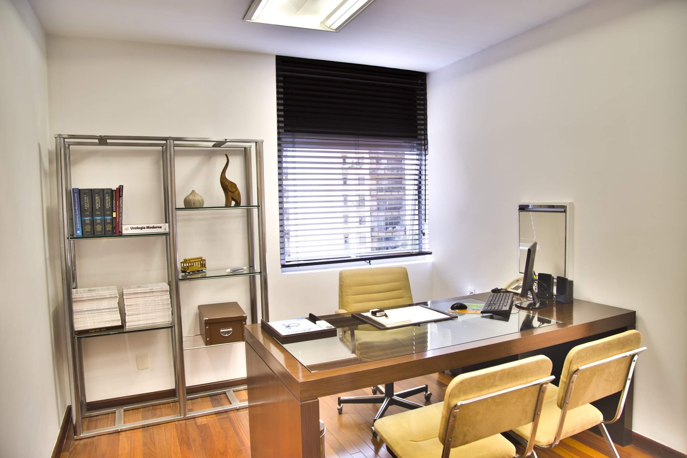 Modern office interior with desk, chairs, bookshelf, and window blinds, creating a professional workspace atmosphere.