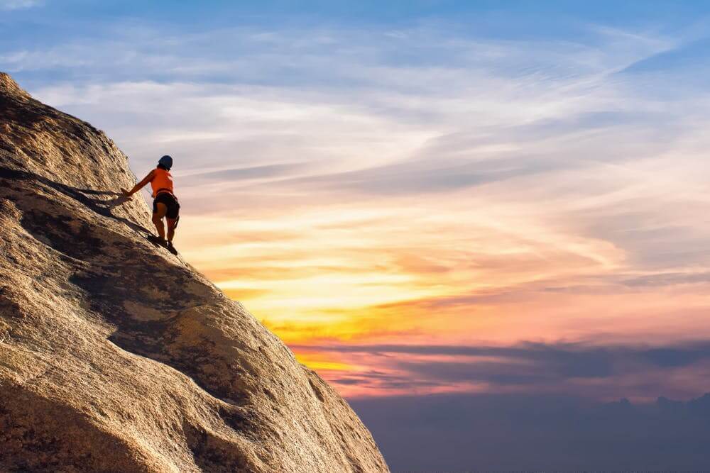 Person rock climbing at sunset, reaching the summit. Adventure and perseverance in nature's stunning landscape.