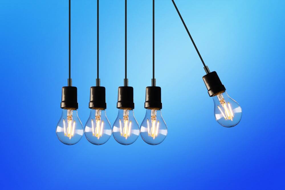 Five hanging light bulbs against a blue background, one bulb swinging outward, symbolizing innovation and ideas.