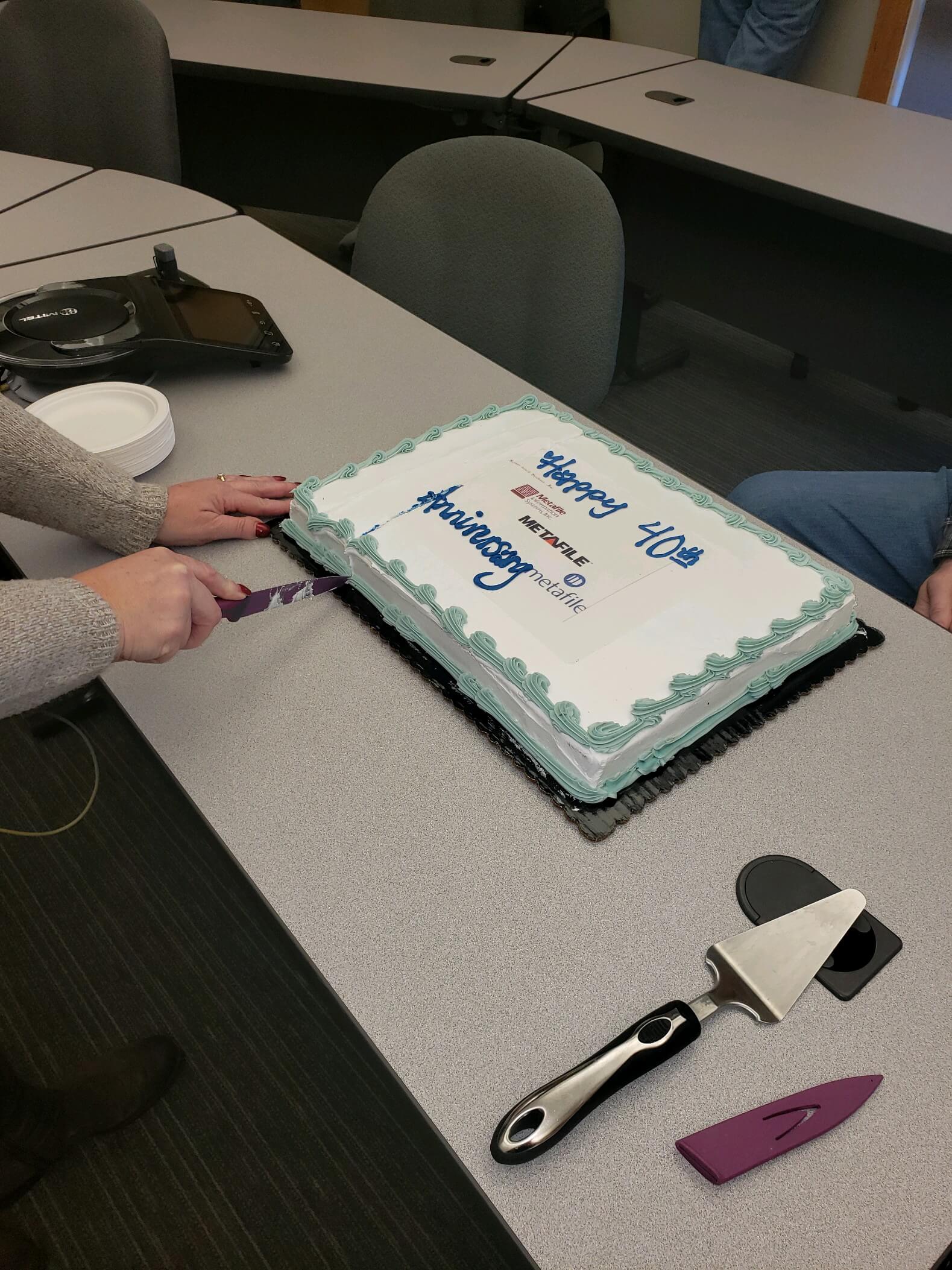 Cutting a 40th anniversary cake in an office setting, celebrating with colleagues.