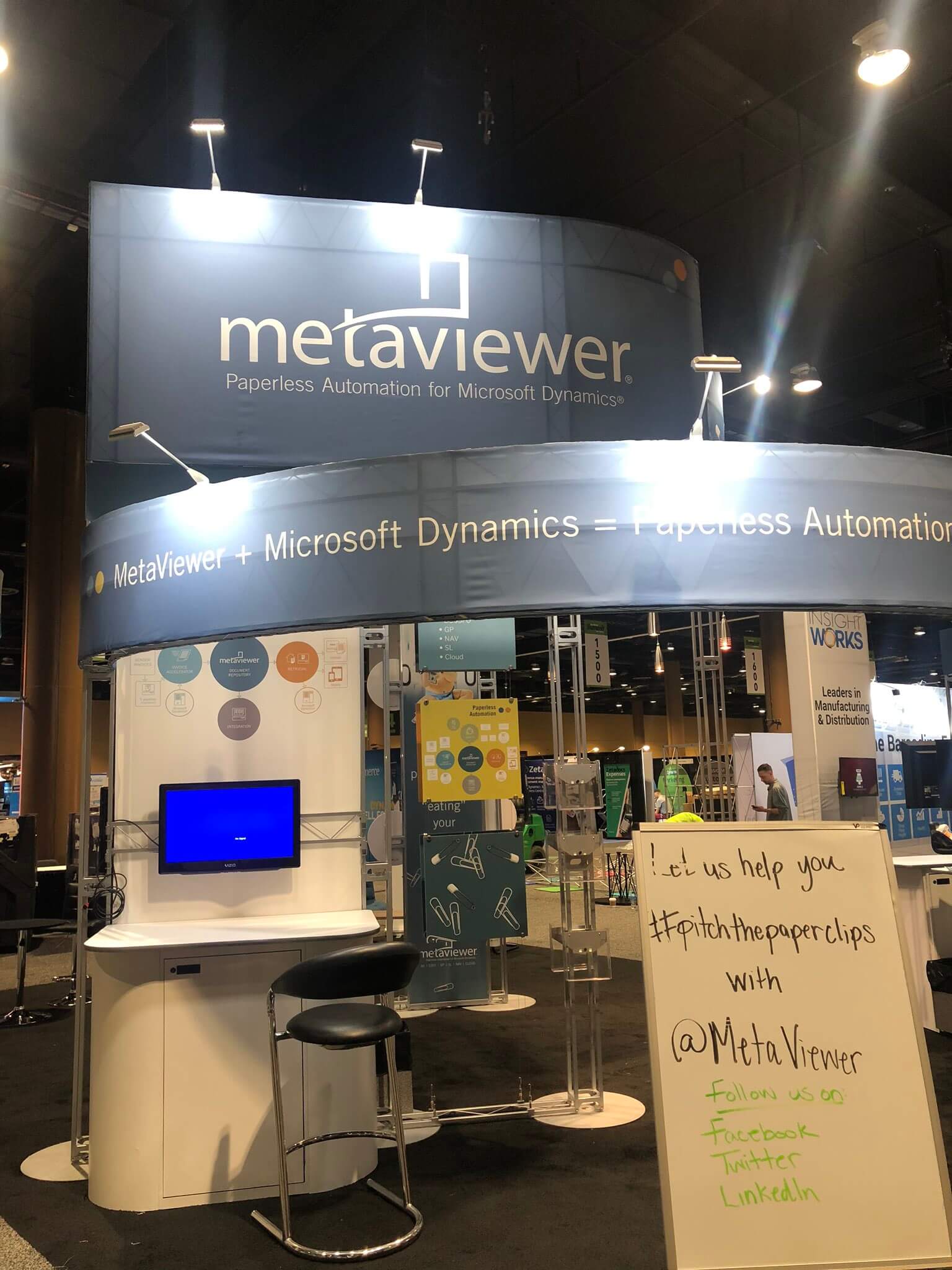 Exhibition booth promoting MetaViewer, showcasing paperless automation for Microsoft Dynamics, with social media hashtag.