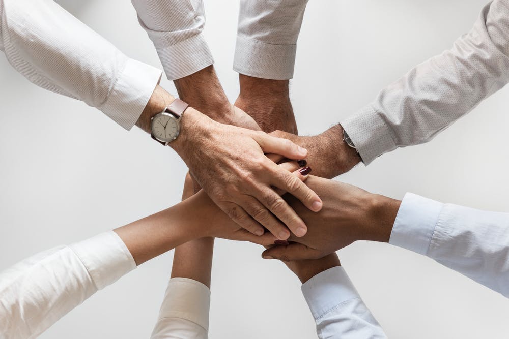 Hands of diverse people stacked together, symbolizing teamwork and unity in a collaborative effort.