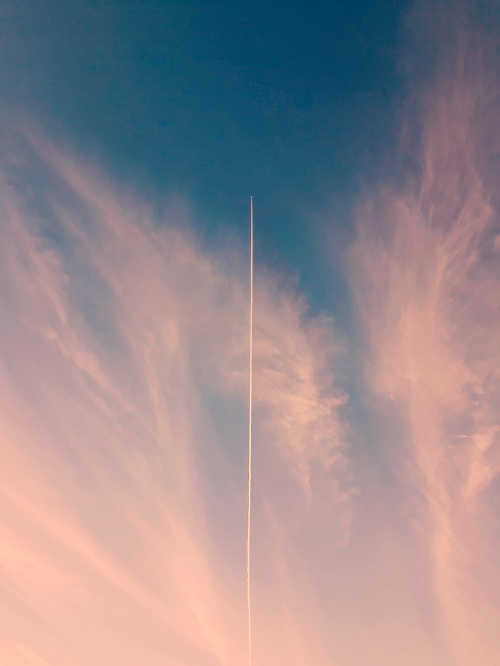 Rocket launching into a serene pink and blue sky with wispy clouds, showcasing a trail of vapor.