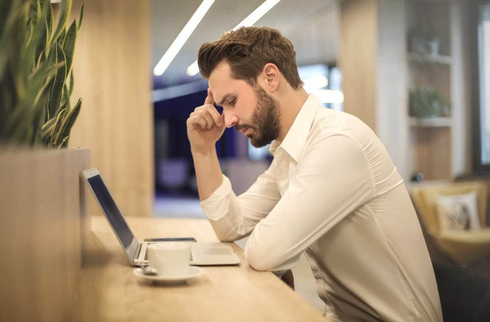 Man in white shirt focused on laptop work at cozy cafe.