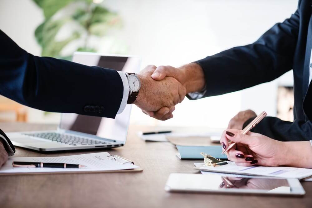 Business handshake over a desk with a laptop and documents, symbolizing successful deal and partnership.
