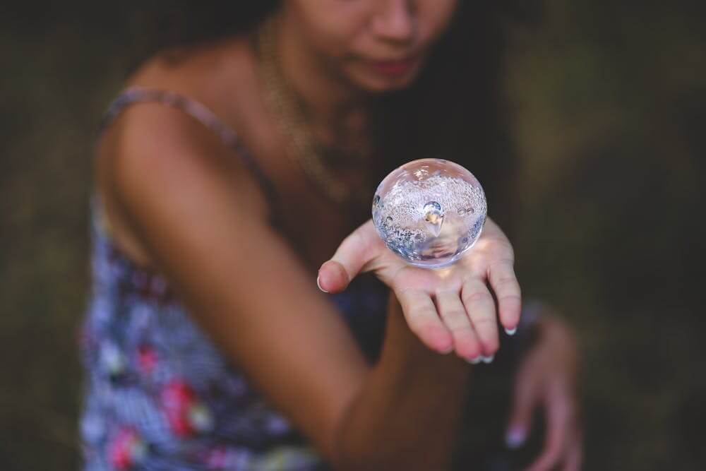 Woman holding a clear bubble sphere in her outstretched hand, wearing a colorful dress, outdoors.