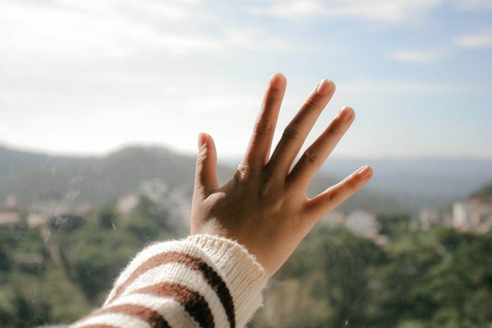 Hand touching window with blurred scenic view of mountains and green landscape in background.