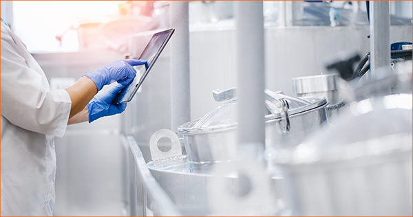 Lab technician using a tablet to monitor industrial equipment and machinery in a laboratory setting.