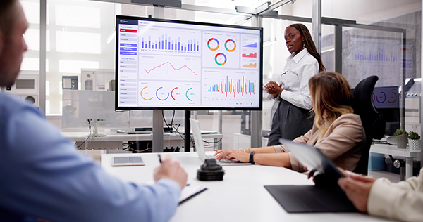 Business presentation with diverse team discussing analytics displayed on a large screen in a modern office setting.