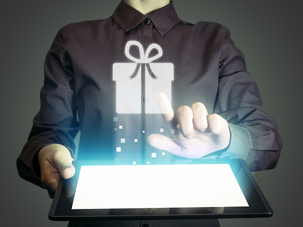 Person interacting with tablet showing a holographic gift box icon, symbolizing digital gifting or online shopping.