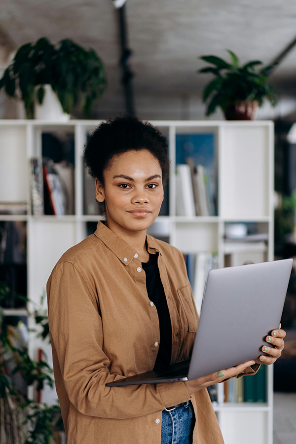 Person holding a laptop in a modern office setting with plants and shelves in the background.