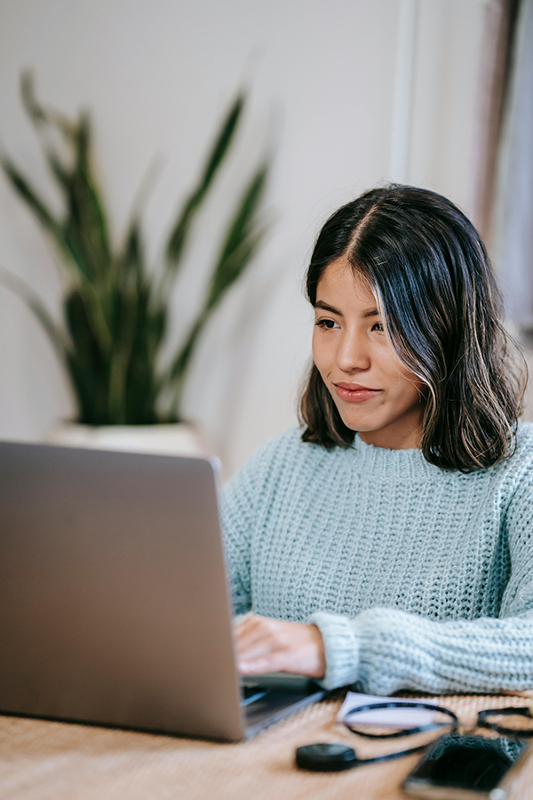 Young woman in blue sweater using laptop at home office, focused and working.
