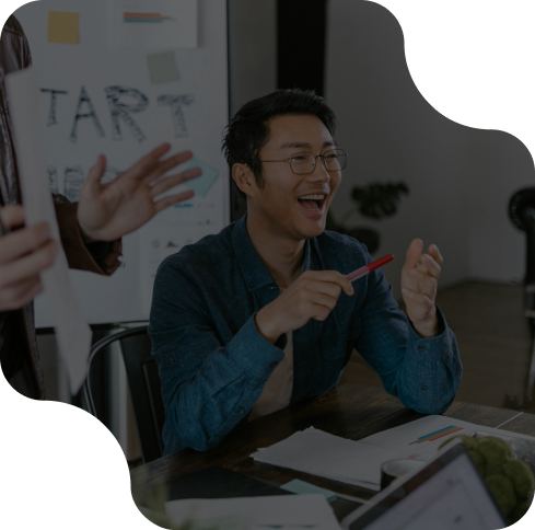 Man smiling during a team meeting, holding a pen, with a whiteboard in the background. Office collaboration concept.