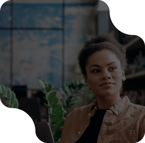 Young professional in a modern office setting, sitting thoughtfully near green plants and shelves.