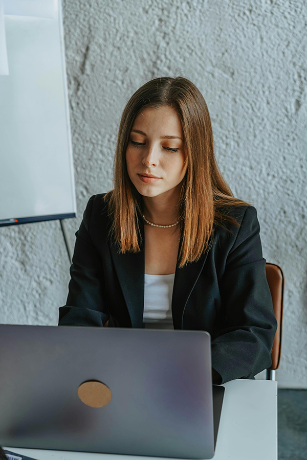 Woman in business attire working on a laptop in an office setting.