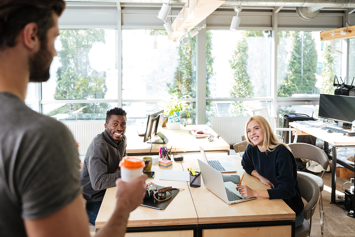 Team collaboration in a modern office with colleagues smiling and using laptops.