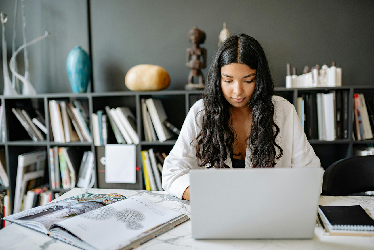 Woman working on a laptop in a stylish office with bookshelves.