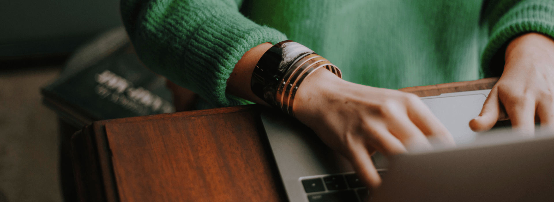 Person in green sweater typing on a laptop, focusing on productivity and technology.