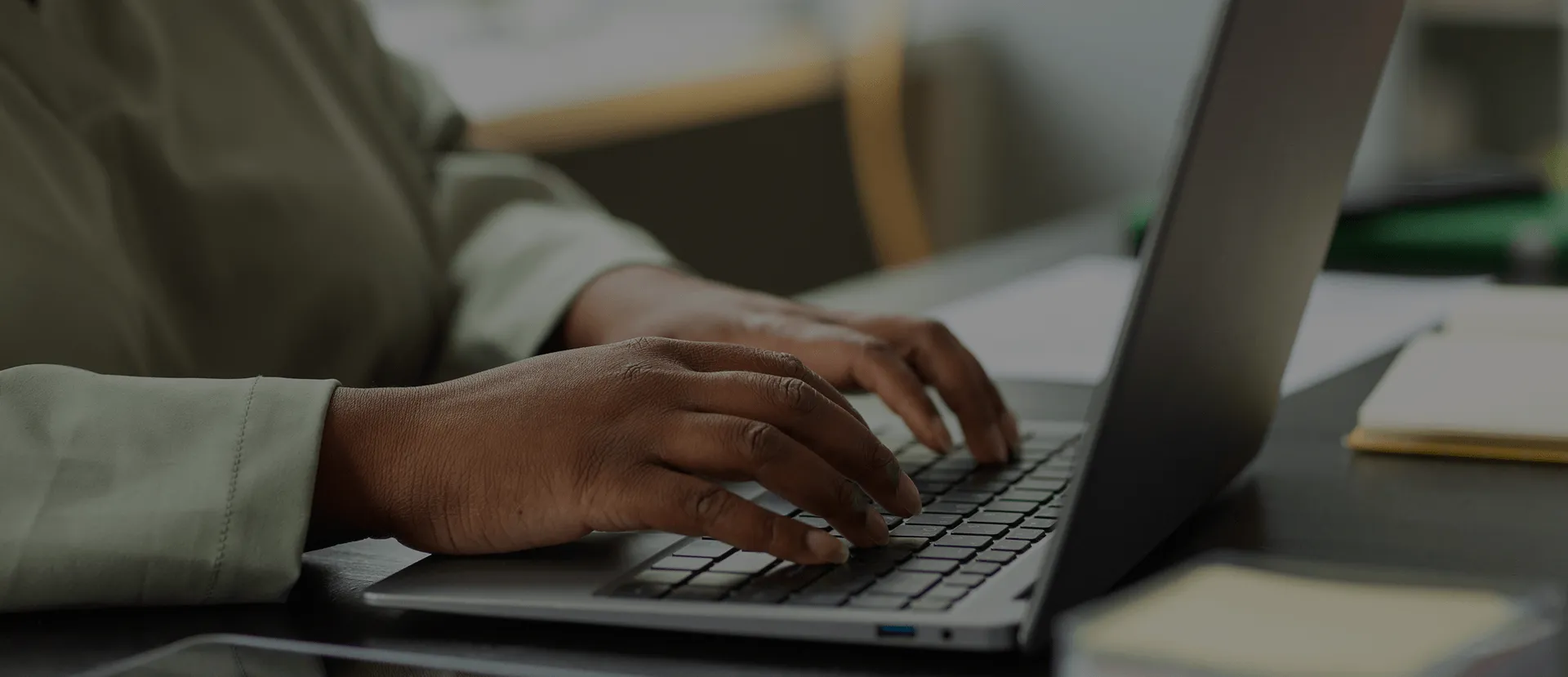 Close-up of hands typing on a laptop keyboard in a dimly lit office setting.