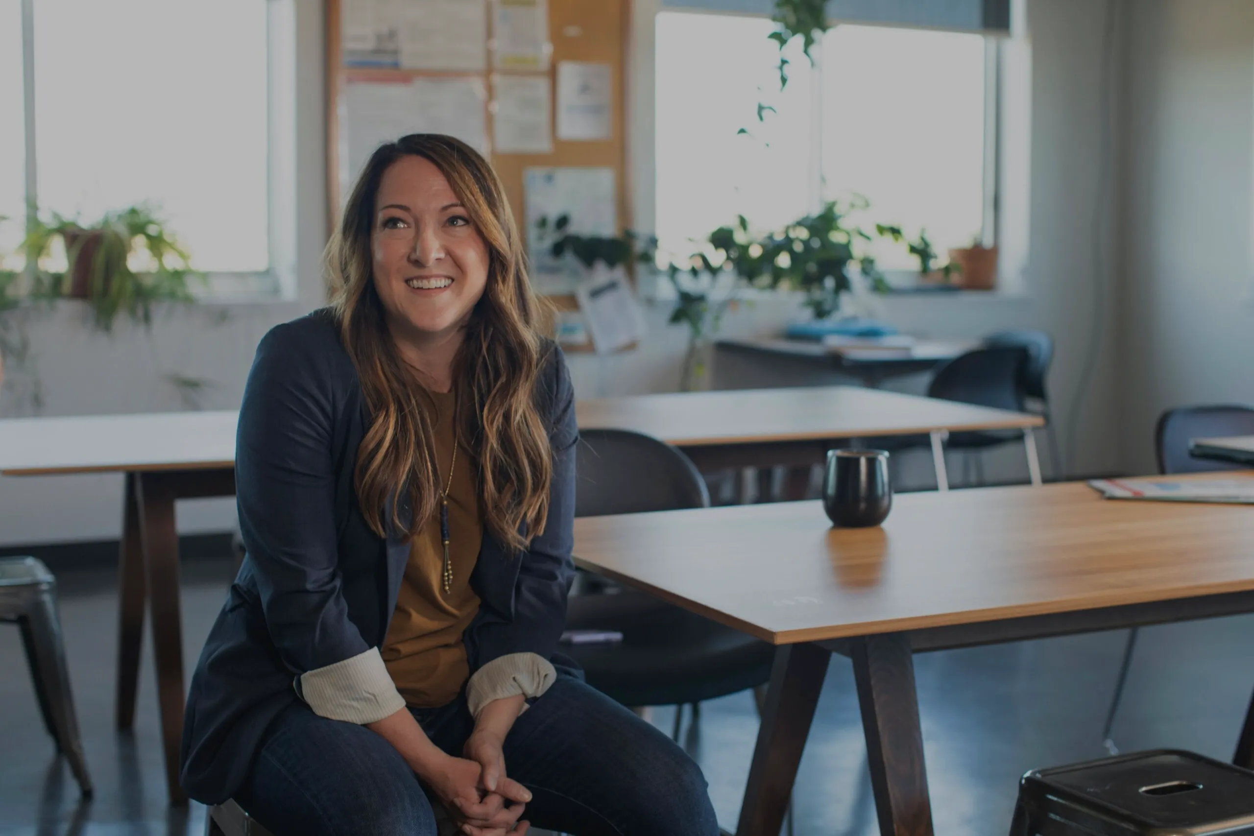 Smiling woman sitting in a modern office setting with plants and natural light.