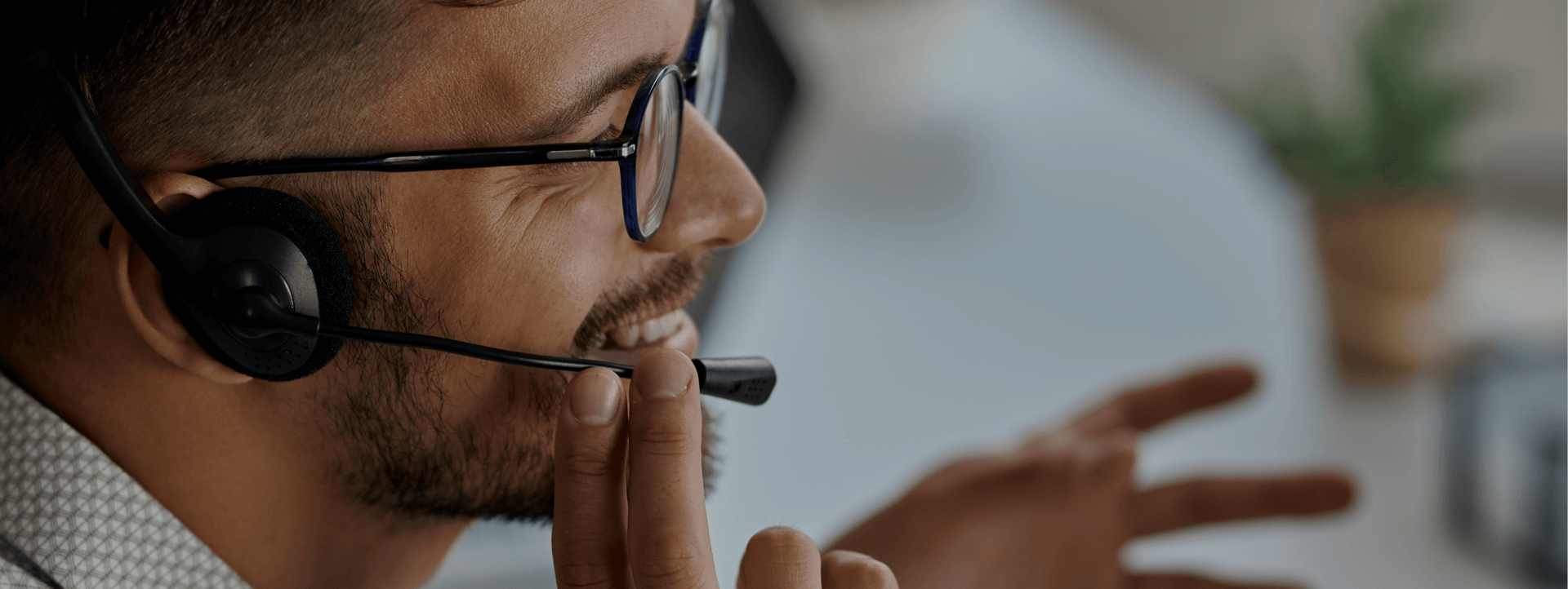 Smiling customer service agent with headset assisting a client over the phone in a modern office setting.